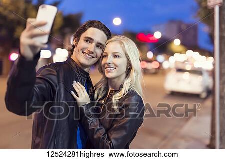 A young couple take a self-portrait with a smart phone along a street at dusk; Edmonton, Alberta, Canada View Large Photo Image Stock Photograph - A young couple take a self-portrait with a smart phone along a street at dusk; Edmonton, Alberta, Canada. Fotosearch