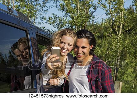 A young couple taking a self-portrait with their smart phone at their vehicle; Edmonton, Alberta, Canada View Large Photo Image Stock Photograph - A young couple taking a self-portrait with their smart phone at their vehicle; Edmonton, Alberta, Canada. Fotosearch