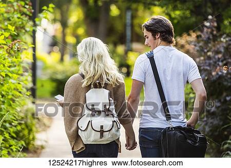 A young couple walking down a path on the university campus holding hands and the woman is checking her smart phone for messages; Edmonton, Alberta, Canada View Large Photo Image Stock Photograph - A young couple walking down a path on the university campus holding hands and the woman is checking her smart phone for messages; Edmonton, Alberta, Canada. Fotosearch