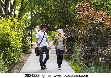 Stock Photograph - A young couple walking down a path on the university campus holding hands and talking; Edmonton, Alberta, Canada. Fotosearch