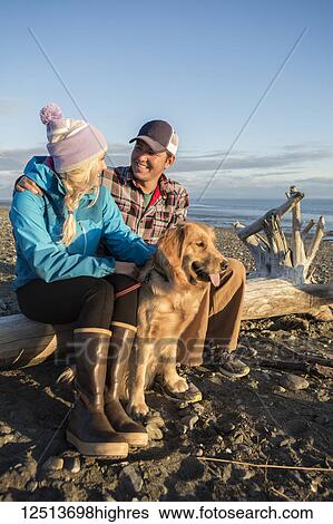 A young couple with their dog sit on a piece of driftwood on a beach at sunset; Anchorage, Alaska, United States of America View Large Photo Image Stock Photograph - A young couple with their dog sit on a piece of driftwood on a beach at sunset; Anchorage, Alaska, United States of America. Fotosearch
