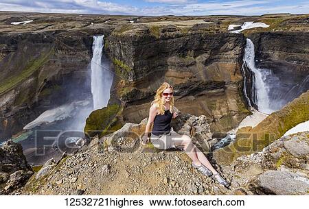 Stock Photograph - A young female hiker poses for a portrait on the edge of a stunning waterfall valley known as Haifoss, in Southern Iceland; Iceland. Fotosearch