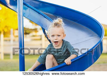 Stock Photograph - A young girl with blond hair playing in a playground and going down a slide on a warm fall day; Spruce Grove, Alberta, Canada. Fotosearch