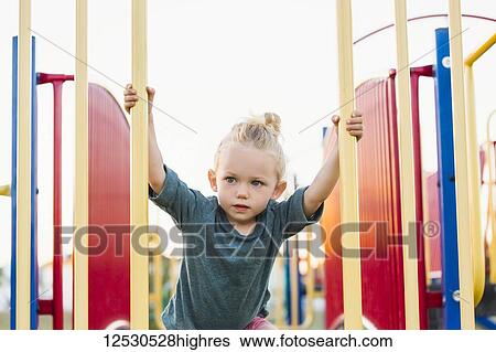 Stock Photograph - A young girl with blond hair playing in a playground and climbing up a rock ladder on a warm fall day; Spruce Grove, Alberta, Canada. Fotosearch