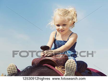 A young girl with curly blond hair sits in the saddle of a horse; Edmonton, Alberta, Canada View Large Photo Image Stock Photograph - A young girl with curly blond hair sits in the saddle of a horse; Edmonton, Alberta, Canada. Fotosearch
