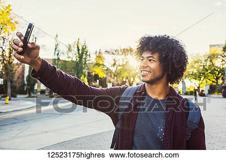 Stock Photograph - A young male African American university student poses for a self-portrait with his smart phone; Edmonton, Alberta, Canada. Fotosearch