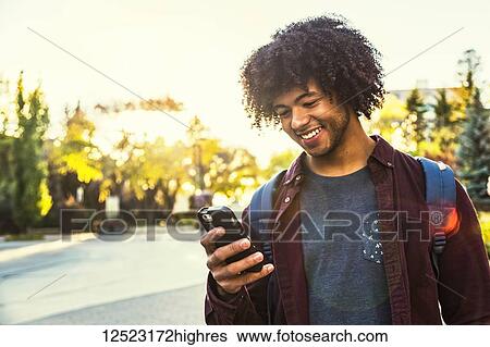 A young male African American student stands using his smart phone on a university campus; Edmonton, Alberta, Canada View Large Photo Image Stock Photograph - A young male African American student stands using his smart phone on a university campus; Edmonton, Alberta, Canada. Fotosearch
