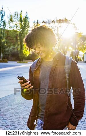 Stock Photograph - A young male African American student stands using his smart phone on a university campus; Edmonton, Alberta, Canada. Fotosearch