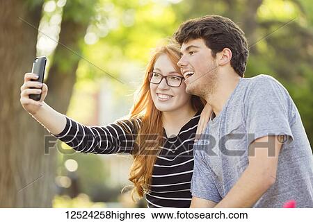 Stock Photograph - A young man and young woman taking a self-portrait on a smart phone; Edmonton, Alberta, Canada. Fotosearch