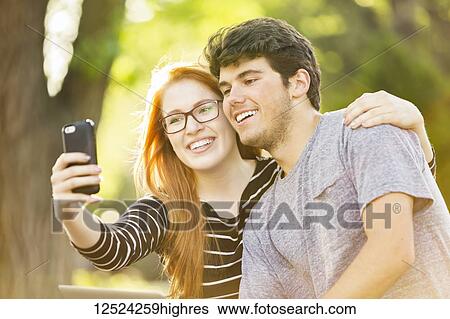 Stock Photograph - A young man and young woman taking a self-portrait on a smart phone; Edmonton, Alberta, Canada. Fotosearch