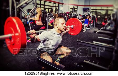 Stock Photograph - A young man doing squat lifts during his weight resitance training at a fitness facility; Spruce Grove, Alberta, Canada. Fotosearch