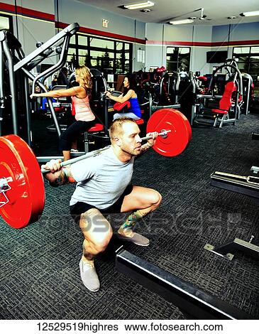 Stock Photograph - A young man doing squat lifts during his weight resitance training at a fitness facility; Spruce Grove, Alberta, Canada. Fotosearch