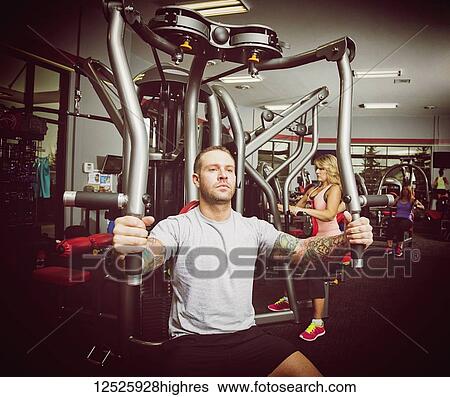 Stock Photograph - A young man working out at a fitness facility using a chest fly cable machine to build up his pectoral muscles; Spruce Grove, Alberta, Canada. Fotosearch