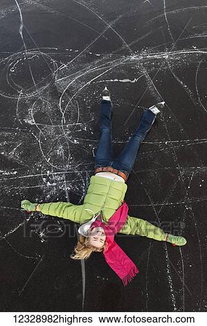 Stock Photograph - A young woman lays on her back on a frozen surface looking up while ice skating; Alaska, United States of America. Fotosearch