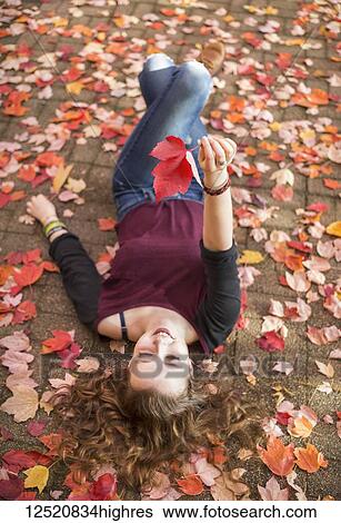 A young woman lays on the ground on colourful fallen autumn leaves; New Westminster, British Columbia, Canada View Large Photo Image Stock Photograph - A young woman lays on the ground on colourful fallen autumn leaves; New Westminster, British Columbia, Canada. Fotosearch