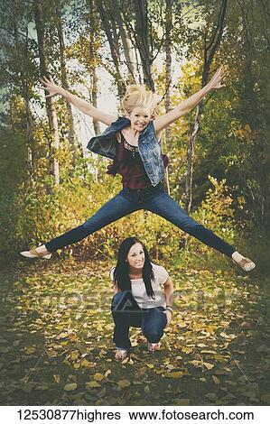 A young woman leaping high in the air over her friend in a park during the fall season; Edmonton, Alberta, Canada View Large Photo Image Stock Photograph - A young woman leaping high in the air over her friend in a park during the fall season; Edmonton, Alberta, Canada. Fotosearch