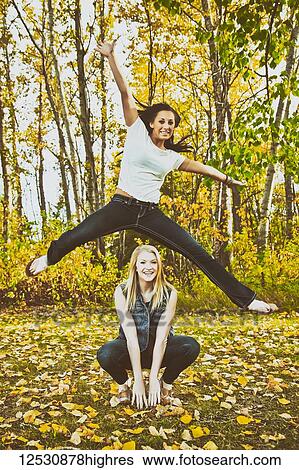 A young woman leaping high in the air over her friend in a park during the fall season; Edmonton, Alberta, Canada View Large Photo Image Stock Photograph - A young woman leaping high in the air over her friend in a park during the fall season; Edmonton, Alberta, Canada. Fotosearch