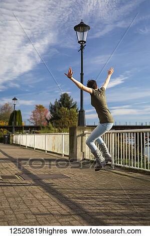 A young woman leaps in the air with arms outstretched on a trail in a park; New Westminster, British Columbia, Canada View Large Photo Image Stock Photograph - A young woman leaps in the air with arms outstretched on a trail in a park; New Westminster, British Columbia, Canada. Fotosearch