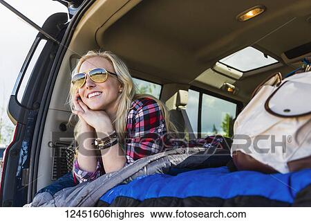 A young woman on a road trip lays in the back of a vehicle with a sleeping bag looking out from the open door; Edmonton, Alberta, Canada View Large Photo Image Stock Photograph - A young woman on a road trip lays in the back of a vehicle with a sleeping bag looking out from the open door; Edmonton, Alberta, Canada. Fotosearch