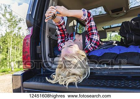 A young woman on a road trip lays in the back of a vehicle with a sleeping bag using her smart phone; Edmonton, Alberta, Canada View Large Photo Image Stock Photograph - A young woman on a road trip lays in the back of a vehicle with a sleeping bag using her smart phone; Edmonton, Alberta, Canada. Fotosearch