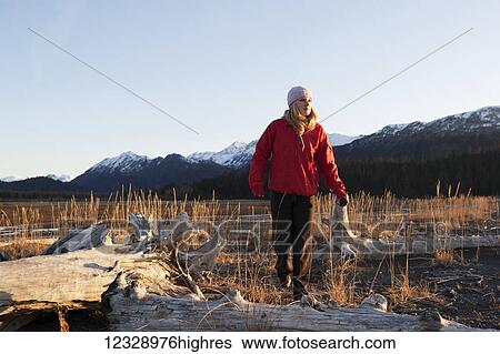 Stock Photograph - A young woman runs past driftwood in Kachemak Bay State Park; Alaska, United States of America. Fotosearch
