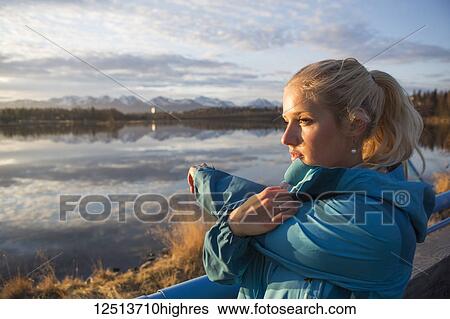 Stock Photograph - A young woman stretching while looking out to the ocean water at sunrise; Anchorage, Alaska, United States of America. Fotosearch
