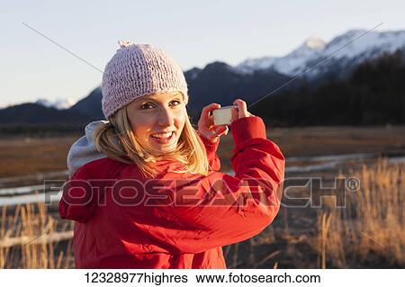 Stock Photograph - A young woman takes a picture of the Kenai mountains in Kachemak Bay State Park; Alaska, United States of America. Fotosearch
