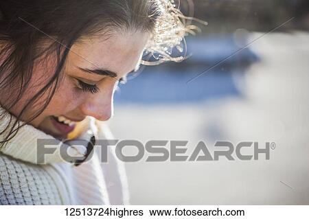 Stock Photograph - A young woman with brown hair looking down and smiling with her hair backlit by the sunlight; Anchorage, Alaska, United States of America. Fotosearch