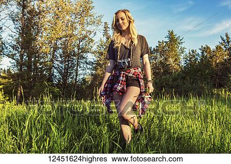 A young woman with long blond hair walks in the grass towards the camera with a camera around her neck; Edmonton, Alberta, Canada View Large Photo Image Stock Photograph - A young woman with long blond hair walks in the grass towards the camera with a camera around her neck; Edmonton, Alberta, Canada. Fotosearch