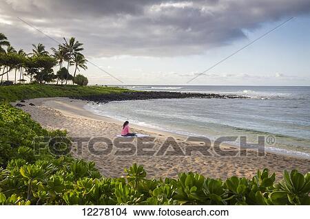 Picture - A young woman works on her computer on a beach in the early morning; Poipu, Kauai, Hawaii, United States of America. Fotosearch