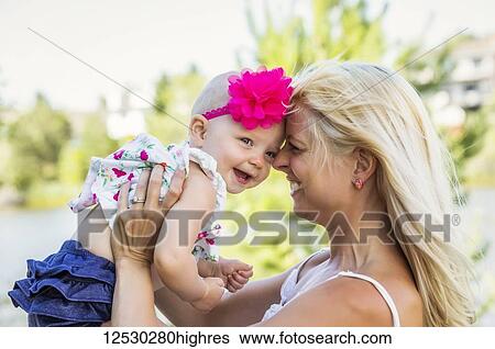 AA beautiful young mother with long blonde hair enjoying quality time with her cute baby daughter in a city park on a summer day; Edmonton, Alberta, Canada View Large Photo Image Stock Photograph - AA beautiful young mother with long blonde hair enjoying quality time with her cute baby daughter in a city park on a summer day; Edmonton, Alberta, Canada. Fotosearch