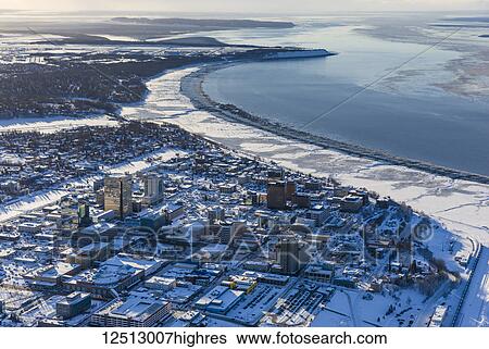 Stock Photograph - Aerial view of snow covering downtown Anchorage and Cook Inlet at low tide, the Hotel Captain Hook and Conoco Philips buildings in the foreground, Fire Island in the distance, South-central Alaska in winter; Anchorage, Alaska, United States of America. Fotosearch
