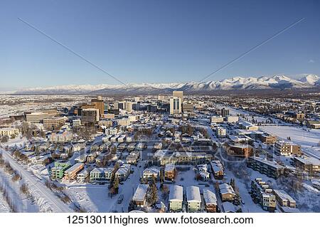 Stock Photograph - Aerial view of snow covering downtown Anchorage and the Chugach Mountains in the distance, the Park Strip and Capitan Cook Hotel visible in the foreground, South-central Alaska in winter; Anchorage, Alaska, United States of America. Fotosearch