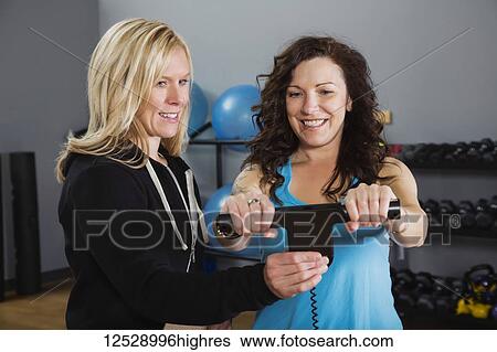 Stock Photograph - An attractive middle-aged woman standing on the scale for her personal trainer after working out at the fitness facility; Spruce Grove, Alberta, Canada. Fotosearch