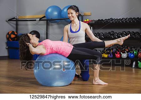 An attractive middle-aged woman working out at the gym using a balance ball with her personal trainer giving assistance; Spruce Grove, Alberta, Canada View Large Photo Image Stock Photograph - An attractive middle-aged woman working out at the gym using a balance ball with her personal trainer giving assistance; Spruce Grove, Alberta, Canada. Fotosearch