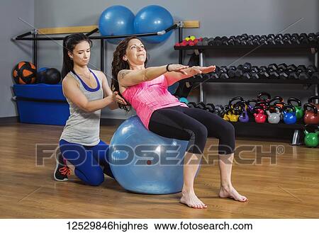 An attractive middle-aged women working out on a balance ball at the gym with her personal trainer giving assistance; Spruce Grove, Alberta, Canada View Large Photo Image Stock Photograph - An attractive middle-aged women working out on a balance ball at the gym with her personal trainer giving assistance; Spruce Grove, Alberta, Canada. Fotosearch