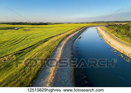 Stock Photograph - An irrigation canal with a path running alongside it and blue sky, East of Calgary; Alberta, Canada. Fotosearch