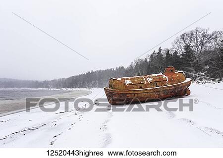 Stock Photograph - An old emergency life-boat safety vessel on the snowy shore in Sandy Cove harbour; Sandy Cove, Nova Scotia, Canada. Fotosearch