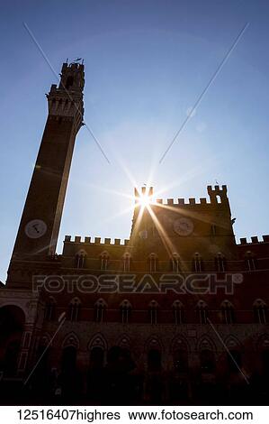 Backlit Palazzo Pubblico (town hall) and Mangia Tower with sunburst and blue sky; Siena, Tuscany, Italy View Large Photo Image Stock Photograph - Backlit Palazzo Pubblico (town hall) and Mangia Tower with sunburst and blue sky; Siena, Tuscany, Italy. Fotosearch