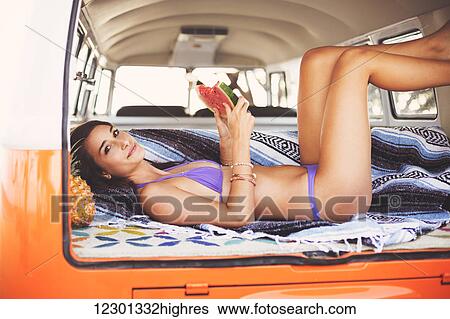 Stock Photograph - Beach Lifestyle, Beautiful Surfer Girl Relaxing Eating Watermelon In Classic Vintage Surf Van. Fotosearch