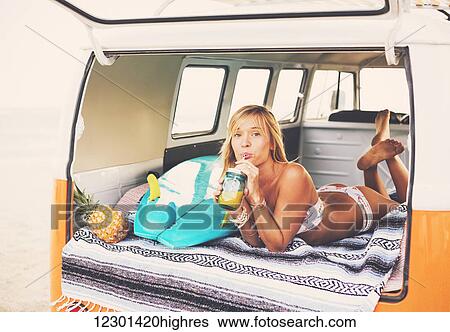 Stock Photograph - Beach Lifestyle, Beautiful Surfer Girl Relaxing In Classic Vintage Surf Van On The Beach At Sunset. Fotosearch