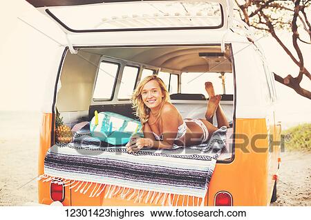Stock Photograph - Beach Lifestyle, Beautiful Surfer Girl Relaxing In Classic Vintage Surf Van On The Beach At Sunset. Fotosearch