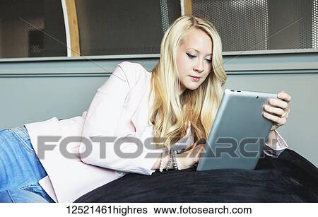 Stock Photograph - Beautiful young millennial business woman with long blond hair in the workplace using a tablet; Sherwood Park, Alberta, Canada. Fotosearch