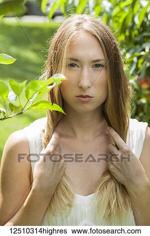 Stock Photograph - Beautiful young woman with long blond hair standing in green foliage; Connecticut, United States of America. Fotosearch
