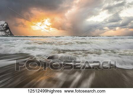 Blur of the tide washing up on the sandy shore along the coast and a golden sun peaking through storm clouds; Nordland, Norway View Large Photo Image Stock Photograph - Blur of the tide washing up on the sandy shore along the coast and a golden sun peaking through storm clouds; Nordland, Norway. Fotosearch