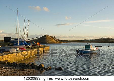 Stock Photograph - Boats in the harbour looking out to St. Cuthbert's cross on a hill along the coast; Alnmouth, Northumberland, England. Fotosearch