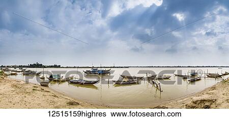 Stock Photograph - Boats moored in the shallow water along the shore; Thanh pho Hoi An, Quang Nam, Vietnam. Fotosearch
