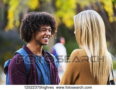Stock Photograph - Boyfriend and girlfriend stand having a conversation and smiling while on the grounds of a university campus; Edmonton, Alberta, Canada. Fotosearch