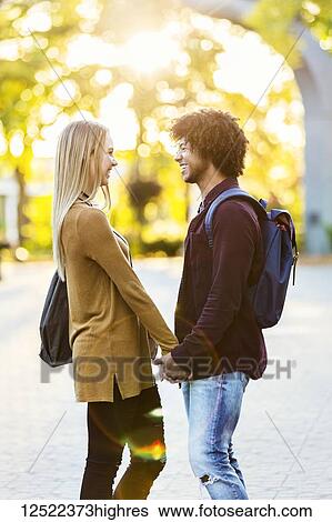Stock Photograph - Boyfriend and girlfriend standing and looking at each other while holding hands on the grounds of a university campus at sunset; Edmonton, Alberta, Canada. Fotosearch