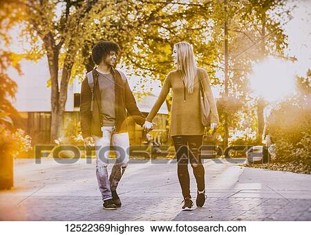 Stock Photograph - Boyfriend and girlfriend walking and holding hands on the university campus at sunset; Edmonton, Alberta, Canada. Fotosearch